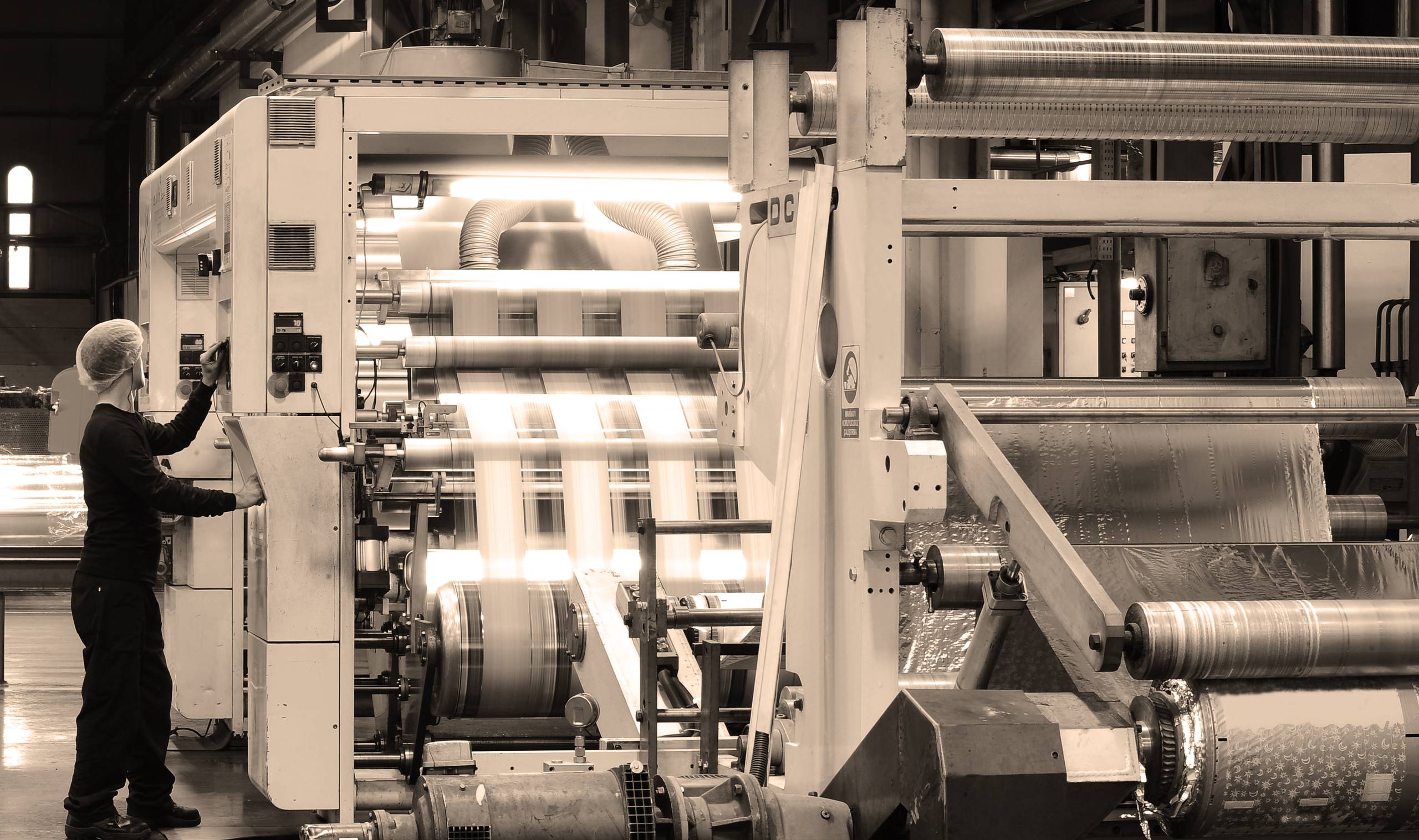A press operator at a large printing machine, printed web running through the rollers